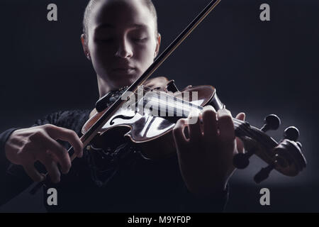 Giovane donna a suonare il violino contro uno sfondo scuro. Studio shot Foto Stock