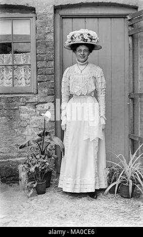 Giovane donna vestita come una damigella in fine l'Inghilterra vittoriana. Indossa occhiali tondi, ed è interamente vestita di bianco, con un elaborato in fiore bianco hat.