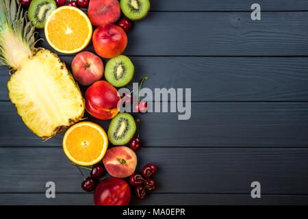 La frutta in legno scuro, tabella. Assortimento di frutta esotica. Vista da sopra con copia spazio. Ananas, pesche, kiwi, agrumi e ciliegio Foto Stock