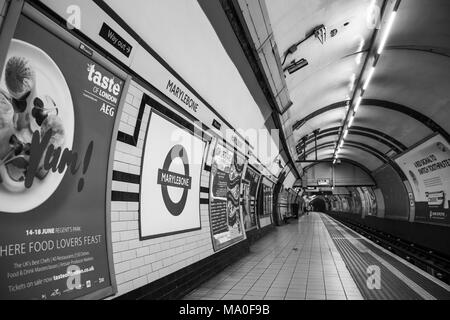 Vista in bianco e nero su una piattaforma deserta della stazione metropolitana di Marylebone. Passeggero isolato in galleria in attesa di treno a metro. Foto Stock