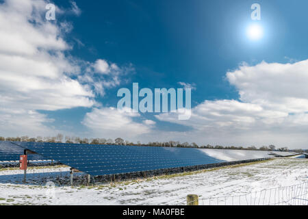 Il sole splende sopra una coperta di neve campo contenente una serie di pannelli solari. Foto Stock