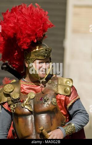 Uomo vestito come un soldato romano, accanto a un banner di militari al di fuori del Colosseo di Roma, Italia. Foto Stock