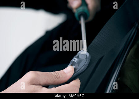 Primo piano di un giovane uomo caucasico cercando di rimuovere un disco di sicurezza tag dalla cinghia di un sacchetto in vendita in un negozio con un cacciavite Foto Stock