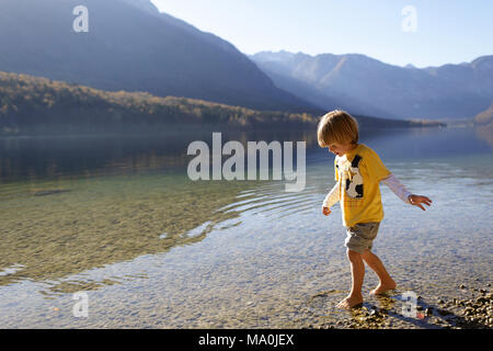 Little Boy giocando a piedi nudi in acqua poco profonda nel lago di Bohinj, Slovenia Foto Stock