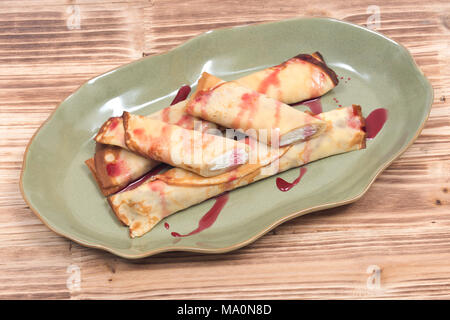 Delizioso formaggio blintz con sciroppo di lampone sulla piastra di verde e legno vassoio vintage isolati su sfondo bianco Foto Stock