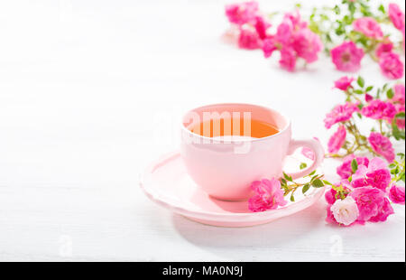 Tazza di tè e la filiale di piccole rose rosa su bianco tavolo rustico. Foto Stock