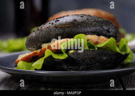 Cucinata fresca hamburger con rotolo di colore nero, verdure e salmone cotoletta. Sandwich fatti in casa closeup Foto Stock