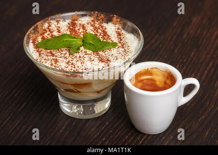 Tiramisù Torta di crema dessert in vetro con le foglie di menta e una tazza di caffè nero su sfondo di legno Foto Stock