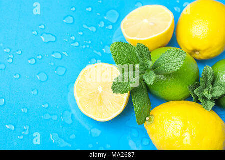 Mature organici di agrumi Limoni Limette intero e dimezzato con menta fresca su fondo azzurro con gocce d'acqua. Luce del sole di mattina. Superfoods Vitami Foto Stock