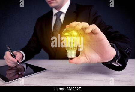 Un business man in tuta in possesso di un giallo brillante lampadina in mano mentre si lavora nel concetto di ufficio. Foto Stock