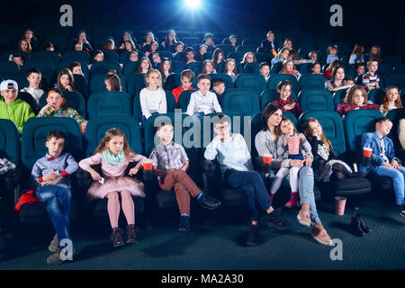 Frontview di persone sedute in sala cinema. I ragazzi e le ragazze la visione di film interessanti e guardando molto emotivo, spaventata e abbandonata. I bambini indossare colorati abiti alla moda. Foto Stock