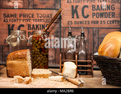 Tagliare il pane fresco su una breadboard in un ristorante con un vaso di olive e bottiglie di olio Foto Stock