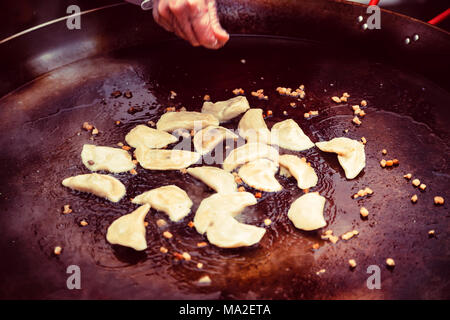 Stretta di mano di uomo cucina russa tradizionale gnocchi vareniki sulla grande padella Foto Stock