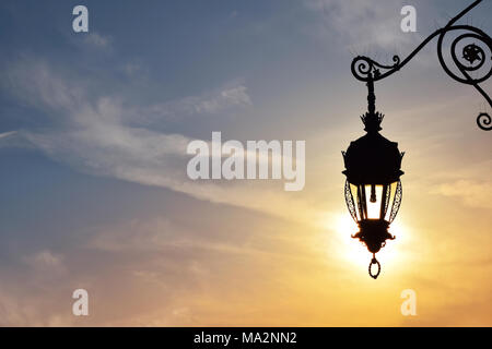 Vicino la vista laterale della vecchia vintage antica strada lampada lanterna brillante sole serale e brillanti Cielo di tramonto Foto Stock