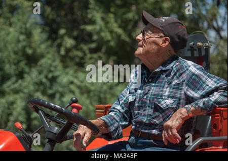 Un sincero ritratto di un senior, maschio agricoltore seduto su un trattore. Foto Stock