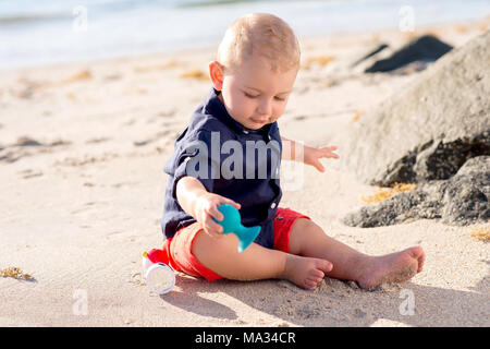 Da un anno un bimbo seduto su di una spiaggia e giocare con un giocattolo. Foto Stock