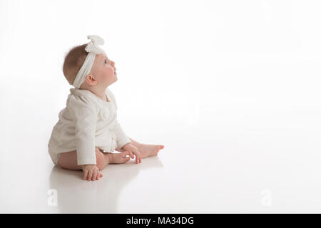 Una vista di profilo di un sorridente, sette mesi di età, bambina indossa bianco. Girato in studio su un bianco, sfondo senza giunture. Foto Stock