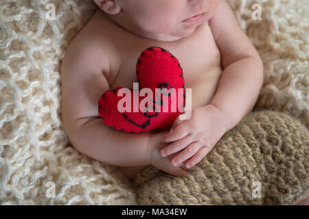 Sei settimane vecchio baby tenendo un cuore Cuscino sagomato con la parola 'amore' scritto su di esso. Foto Stock