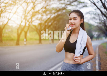 Giovane donna sportiva in appoggio e strofinando il suo sudore con un asciugamano dopo allenamento sport esercizi all'aperto presso il parco Foto Stock