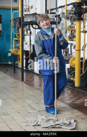 Sorridente vecchia donna il detergente in abbigliamento da lavoro sul sito di fabbricazione Foto Stock