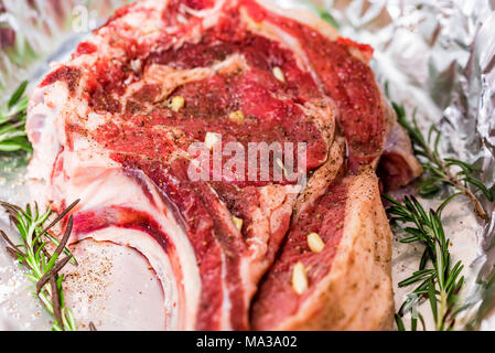 Close-up di bistecca di manzo pronta per la cottura coperto di spezie e farcite con spicchi di aglio Foto Stock