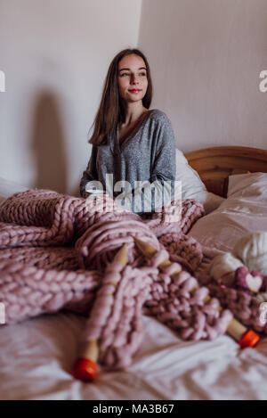 Giovane donna seduta nel letto con una tazza di tè Foto Stock