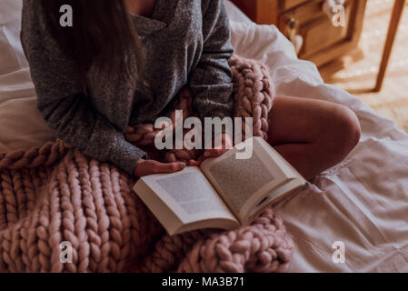 Giovane donna seduta sul letto e la lettura di un libro,dettaglio, Foto Stock