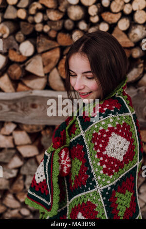 Giovane donna avvolta in una coperta di fronte a woodpile,ritratto Foto Stock