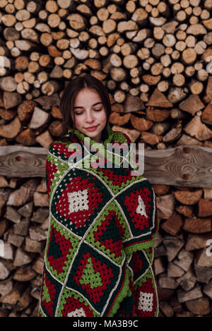 Giovane donna avvolta in una coperta di fronte a woodpile Foto Stock