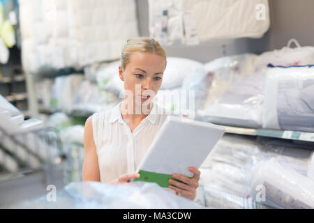 Donna acquistare lenzuola per il suo letto nel moderno arredamento home store. Foto Stock