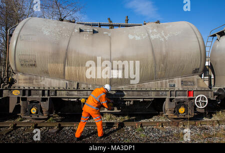 Un operaio ferroviario in hi viz abbigliamento riparazione di un carro cisterna a lato rampa. Foto Stock