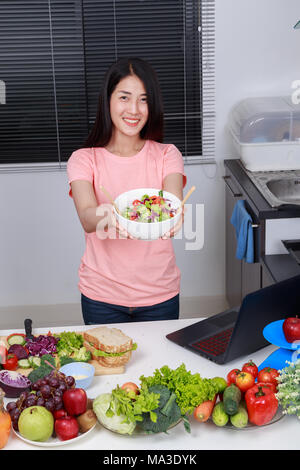 Giovane donna insalata di mescolamento durante la cottura in cucina Foto Stock