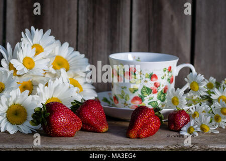 Fragole con chamomiles e una tazza di tè sul vecchio albero sullo sfondo Foto Stock