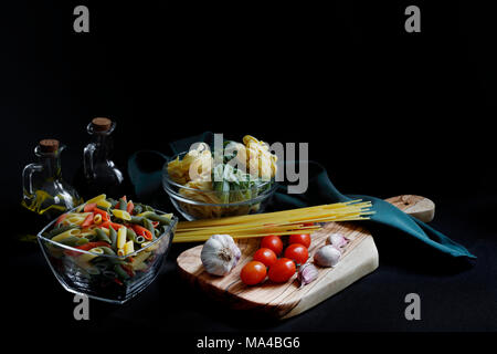 Chiaroscuro scuro Pasta alimentare ingredienti con spaghetti, tagliatelle e penne tricolore e aglio con olio di oliva con spazio coppy Foto Stock