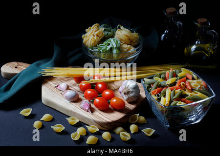 Chiaroscuro scuro Pasta alimentare ingredienti con spaghetti, tagliatelle e penne tricolore e aglio con olio di oliva con spazio di copia Foto Stock