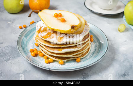 Colazione fatta in casa: american style pancakes servita con frutti di bosco, pera e miele su sfondo di calcestruzzo Foto Stock