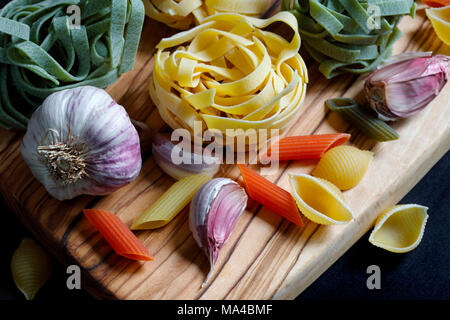 Chiudere fino a chiaroscuro cibo scuro ingredienti per la pasta con gli spaghetti, tagliatelle e penne tricolore e aglio Foto Stock