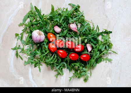 Rucola Foglie di rucola con i pomodorini e aglio per il cibo italiano sulla tavola di marmo Foto Stock