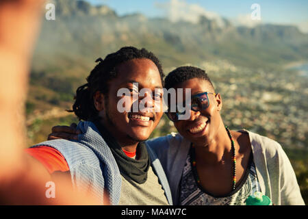 Due maschi felici amici africani prendere un selfie insieme durante le escursioni all'aperto con splendide montagne sullo sfondo e vera emozione nei loro sorrisi Foto Stock