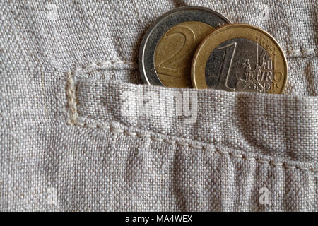 Monete metalliche in euro con una denominazione di uno e due euro in tasca di indossare pantaloni di lino Foto Stock