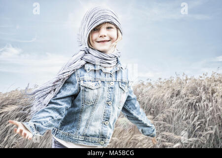Bambina in piedi in un cornfield, contro il vento Foto Stock