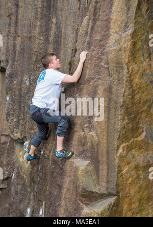 Giovane uomo rock climbing (bouldering) senza corde sulla roccia brunastro. Foto Stock