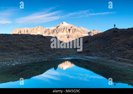 Escursionista in silhouette nei pressi di un laghetto con il gruppo del Sella con il più alto il Piz Boè mountain riflessa, Passo Pordoi, Arabba, Beuuno, Veneto, Italia Foto Stock