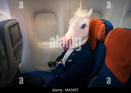 Giovani funny man in maschera viaggi in aereo. Insolito passeggero in tuta si siede da solo a bordo degli aeromobili e pronto al decollo. Freaky traveler unicorn godere battenti Foto Stock