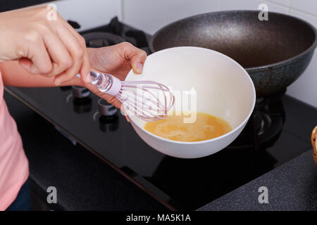 Stretta di mano e cottura sbattere le uova in una ciotola in camera con cucina Foto Stock