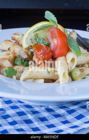 Una ciotola di Penne insalata di pasta, insalata di pasta di Penne. guarnita wirh fresco cuneo di limone e foglie di basilico fresco Foto Stock