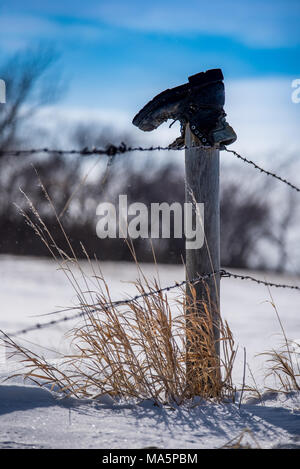 Vecchio boot sulla parte superiore del palo da recinzione a sud di Swift corrente, Saskatchewan, Canada con erba alta inserimenti fuori della neve e il blu del cielo Foto Stock