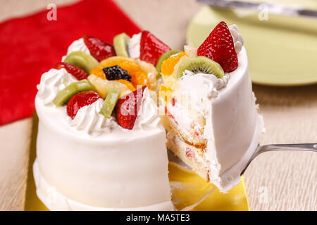 Il sollevamento di una fetta di torta bianca guarnita con frutta fresca. Foto Stock