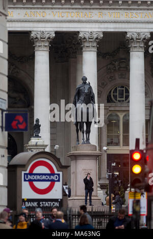 Un uomo fa una chiamata sotto la statua equestre del Duca di Wellington alla stazione della metropolitana di Bank sulla Cornhill nella città di Londra, capitale del distretto finanziario (aka Square Mile), il 26 marzo 2018, a Londra, in Inghilterra. Foto Stock