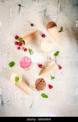 Estate frutti dolci e dessert vari di gusto di gelato in cono rosa (lampone, vaniglia e cioccolato con menta su calcestruzzo leggero sfondo Foto Stock